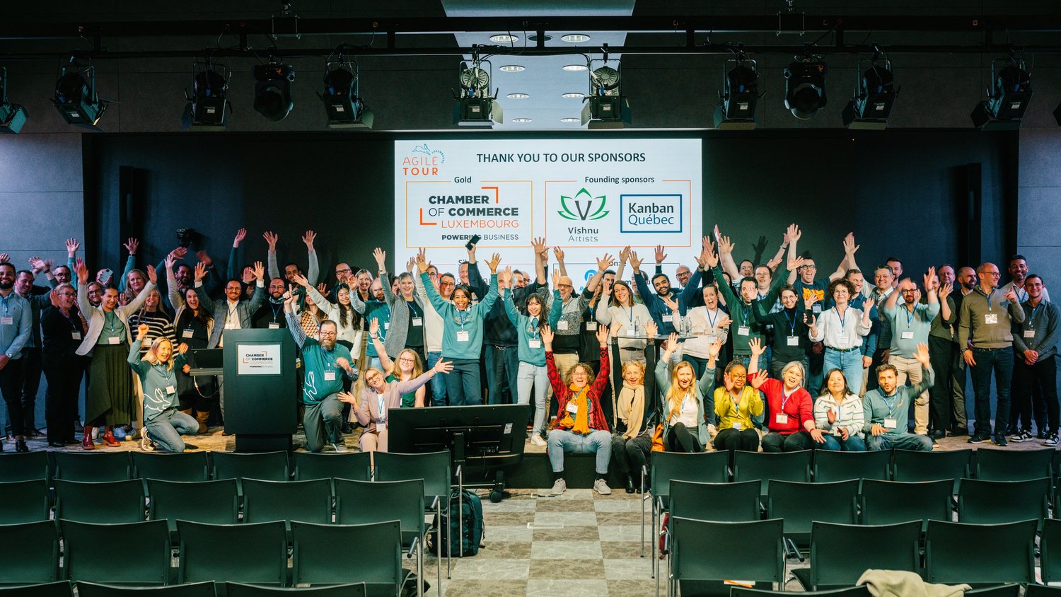 Participants de l’Agile Tour Luxembourg sur scène, bras levés devant la diapositive des sponsors.