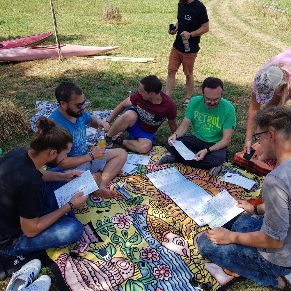 Gruppe sitzt auf einer bunten Decke auf der Wiese und arbeitet mit ausgedruckten Arbeitsblättern.
