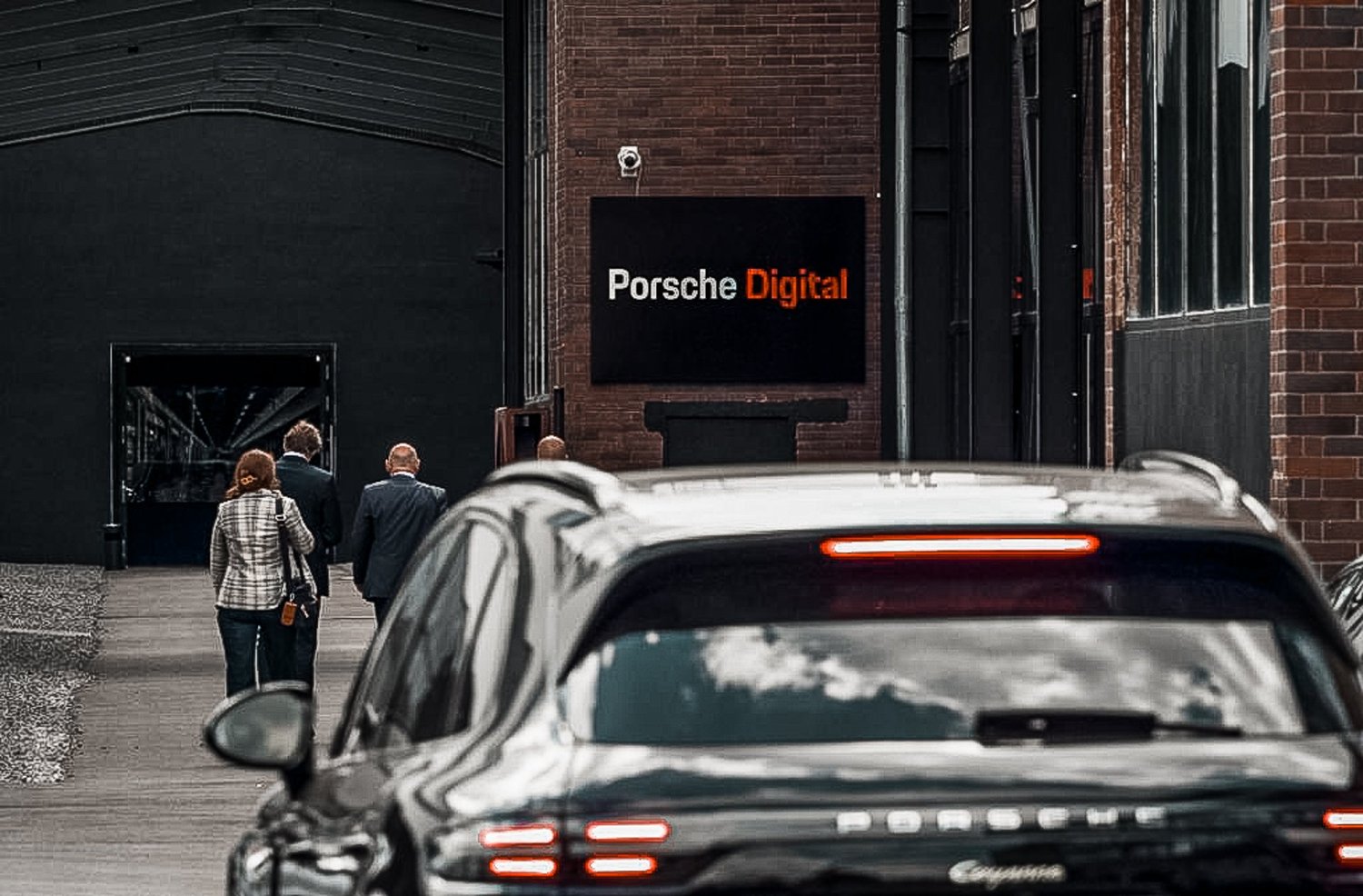 Entrée du bâtiment de Porsche Digital, un Cayenne garé au premier plan.