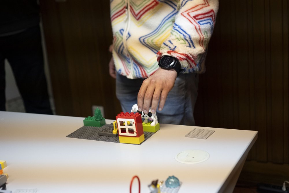 Eine Hand stellt eine LEGO-Kuh neben ein kleines gebautes Haus.
