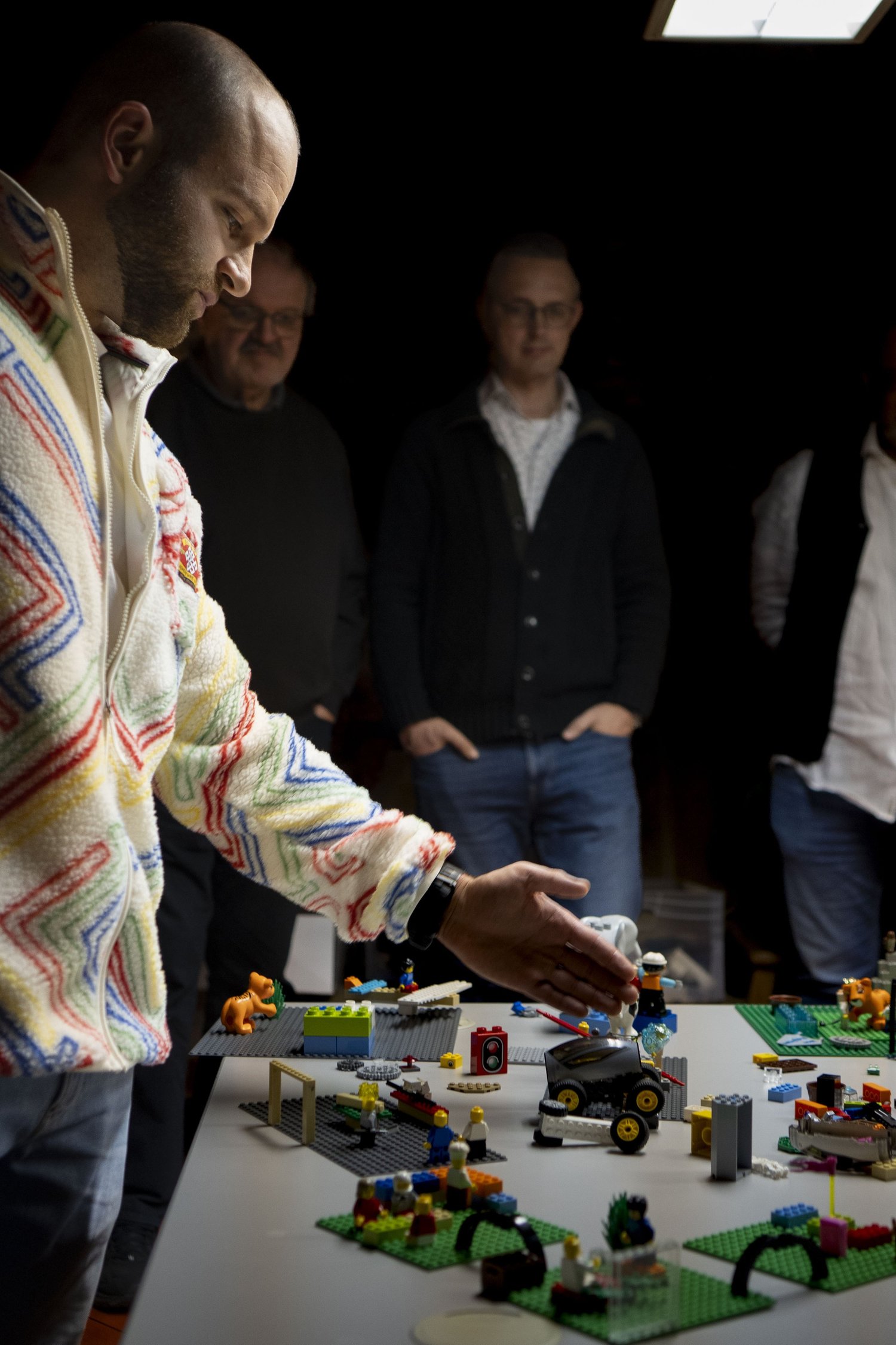 Die Workshopleitung ordnet LEGO-Modelle auf einem Tisch, Teilnehmende schauen zu.