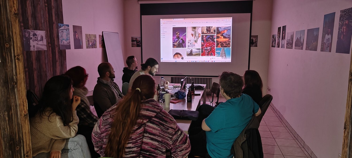 Teilnehmende des Meetups sitzen im Co:Working 66 um einen Tisch und schauen auf KI-erzeugte Bilder an der Projektionswand.