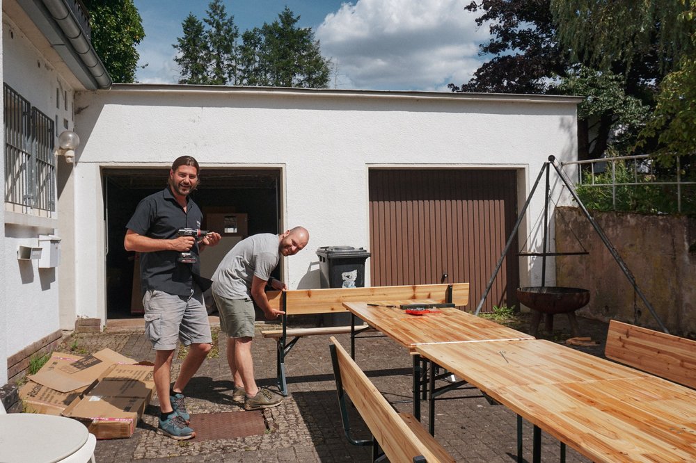 Deux collègues montent des tables de brasserie devant le garage.