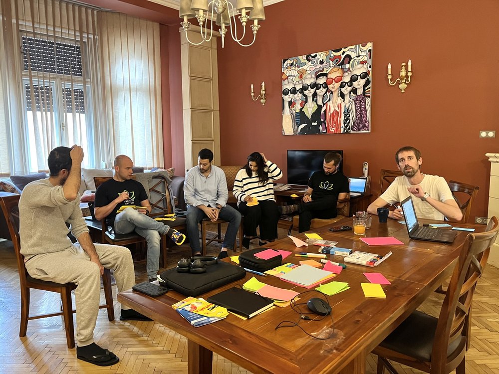 Arbeitsrunde des Teams um einen Esstisch in einer Budapester Wohnung.