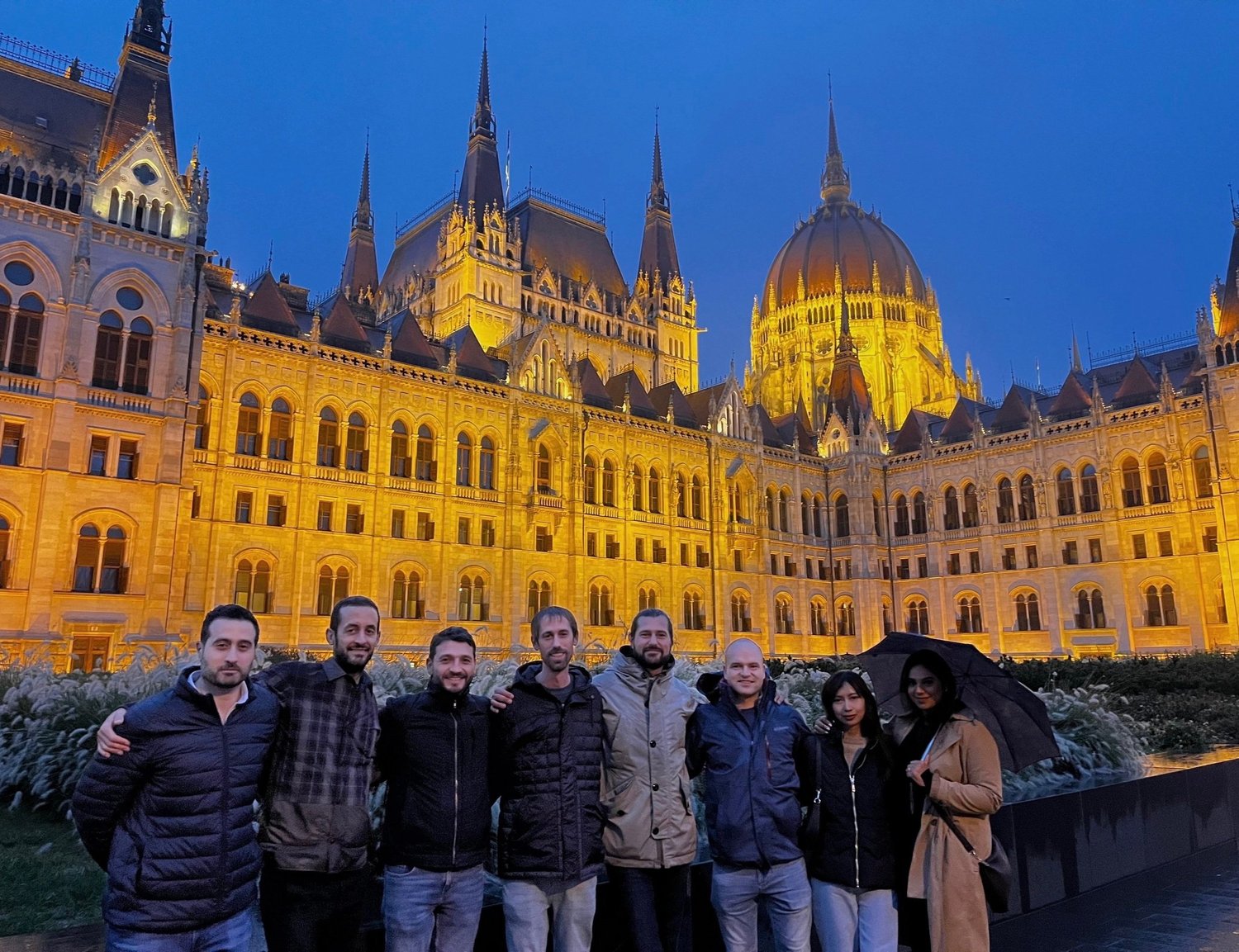 Teamfoto vor dem beleuchteten ungarischen Parlament in der Dämmerung.