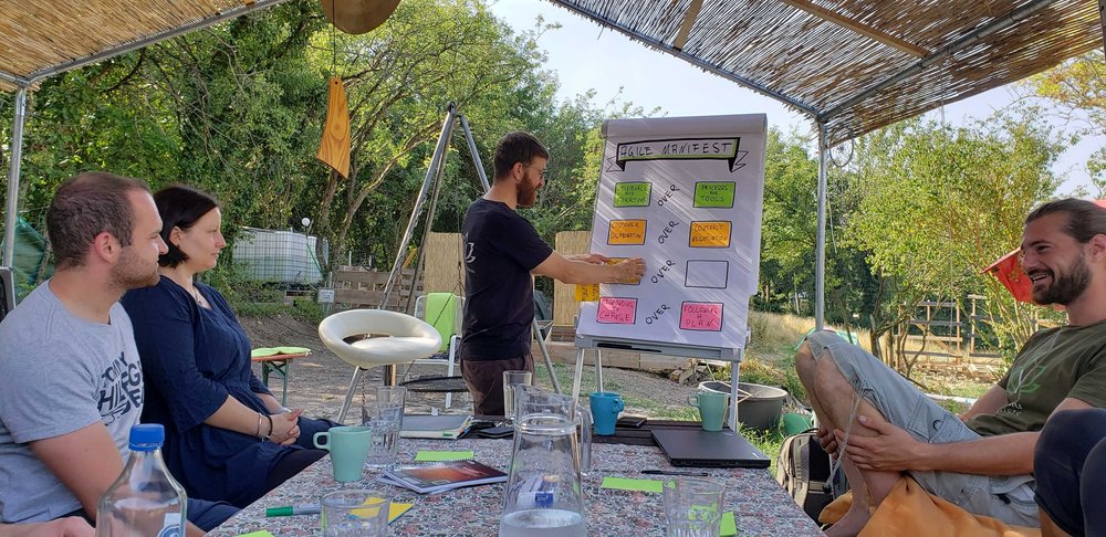 Trainer an einem Flipchart mit dem Agilen Manifest unter einem Reetdach.
